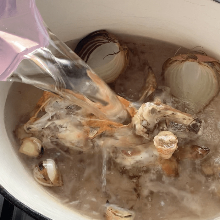 Roasted chicken frame and onion in a pot with water being poured in