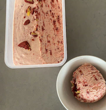 A bowl of Red Velvet Oreo Ice Cream next to a tub of red velvet ice cream with a scoop taken out of it