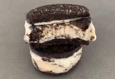 2 Cookies and Cream Ice Cream sandwiches stacked on top of each other sandwiched between oreos, one with a bit out of it