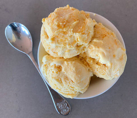 A bowl filled with 3 scoops of mango ice cream with a spoon next to the bowl
