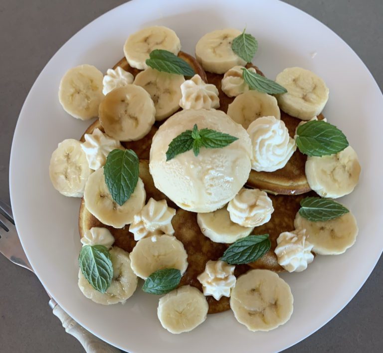 Fluffy American diner Style mini pancakes with sliced banana, vanilla ice cream, fresh mint, whipped cream and maple syrup