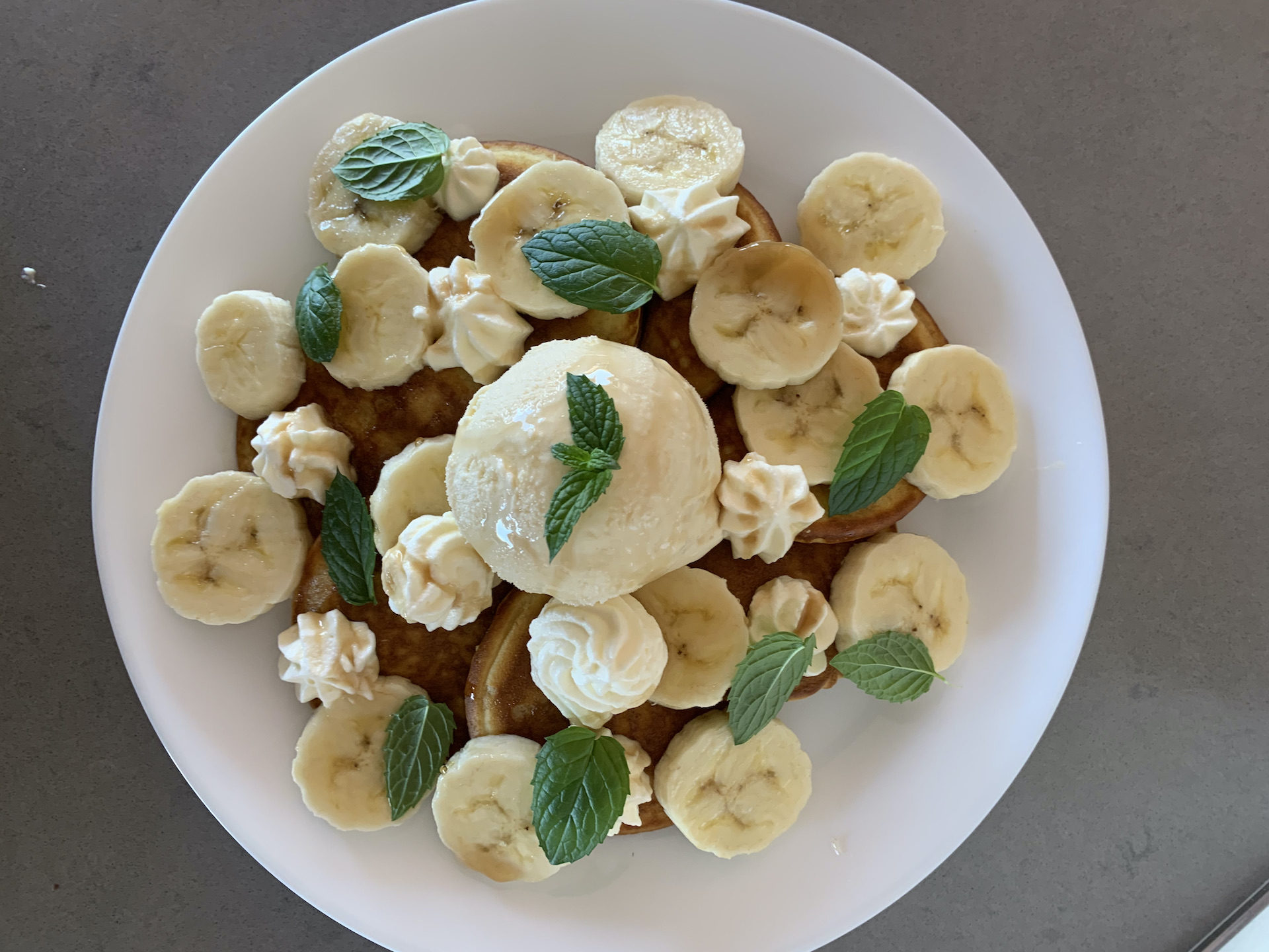 Fluffy American Diner Style mini pancakes with sliced banana, vanilla ice cream, fresh mint, whipped cream and maple syrup