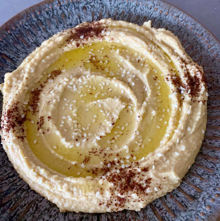 Hummus on a grey plate topped with olive oil, sesame seeds and sumac