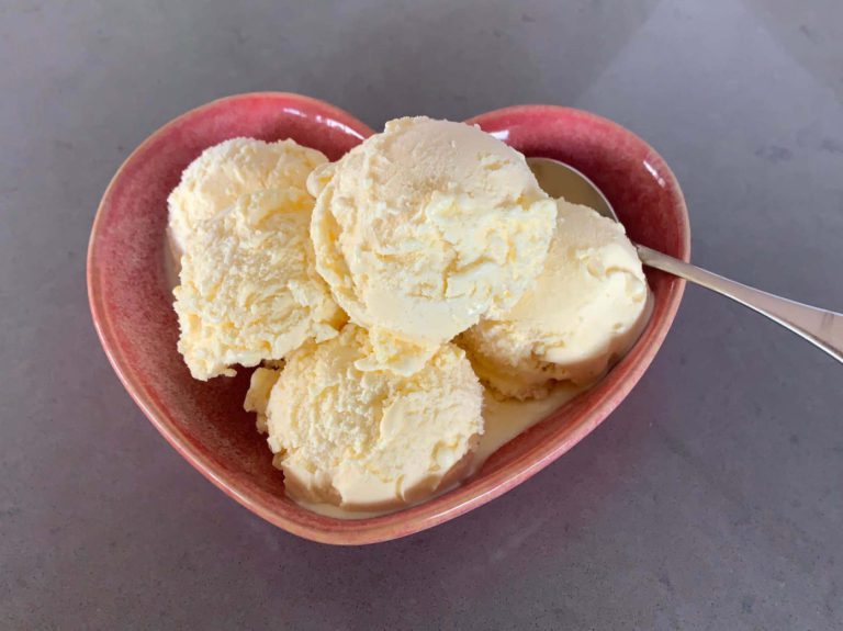 A pink love heart shaped bowl filled with 6 scoops of vanilla ice cream with a teddy bear spoon
