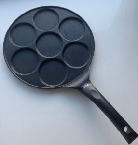 A black non stick pan with 7 individual holes for mini pancakes