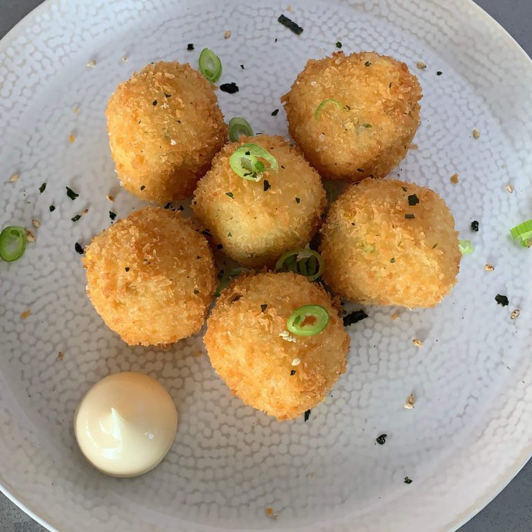 A plate of 6 golden potato croquettes sprinkled with furikake and chopped spring onions with a dollop of mayo on the side