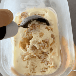 A tub of cornflake ice cream with chunks of cornflakes throughout being scooped