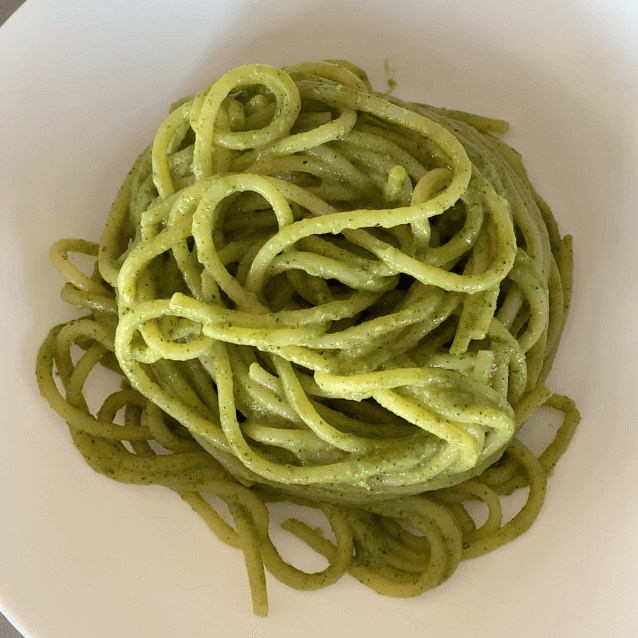A bird eye image of a bowl of spaghetti coated in a bright green sauce in a white bowl