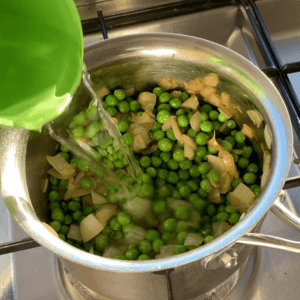 A pot filled with onions and peas with water being poured in from a green measuring cup