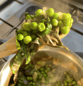 A wooden spoon piled with steaming peas and basil over a silver pot