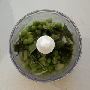 A small food processor filled with peas, basil and onion