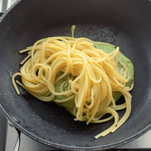 A black frying pan with a green sauce topped with cooked spaghetti