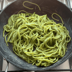 A black frying pan filled with spaghetti coated in a green sauce