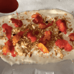 Yoghurt spread on a tray topped with granola and plums, being drizzled with plum syrup