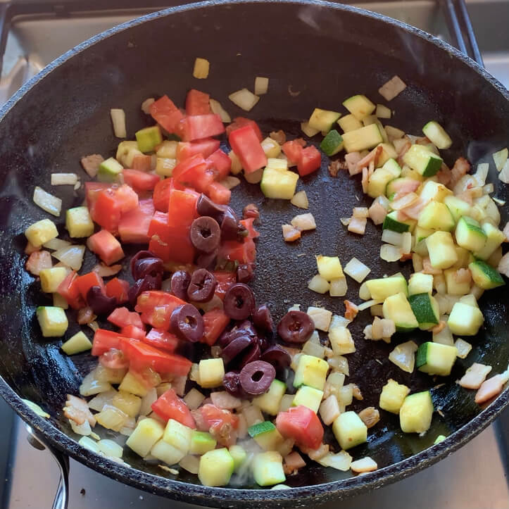diced Zucchini, onion, olives, tomato and bacon in a frypan