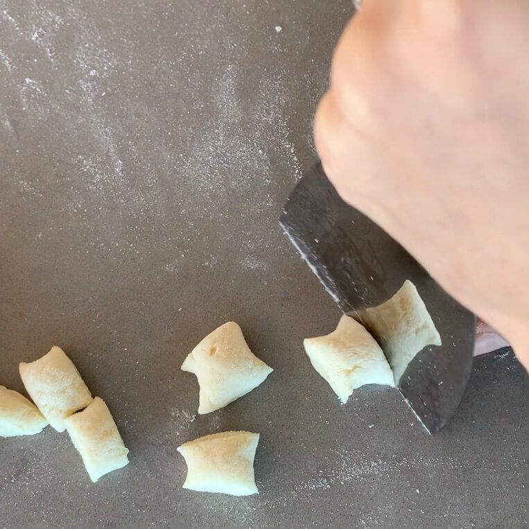 Gnocchi dough being cut with a paint scraper