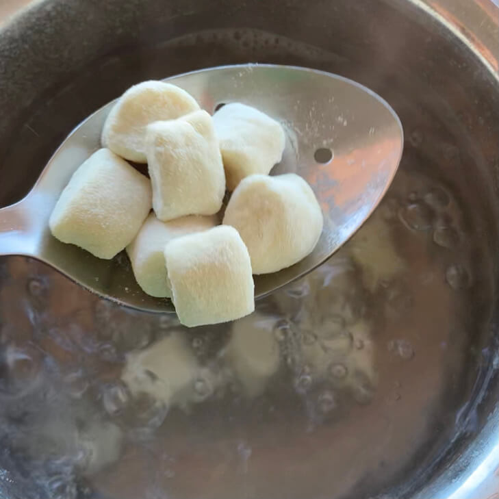 Gnocchi on a spoon being put in boiling water