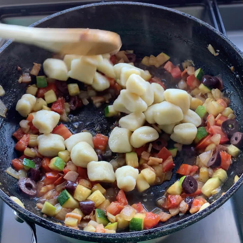 gnocchi with diced Zucchini, onion, olives, tomato and bacon in a frypan