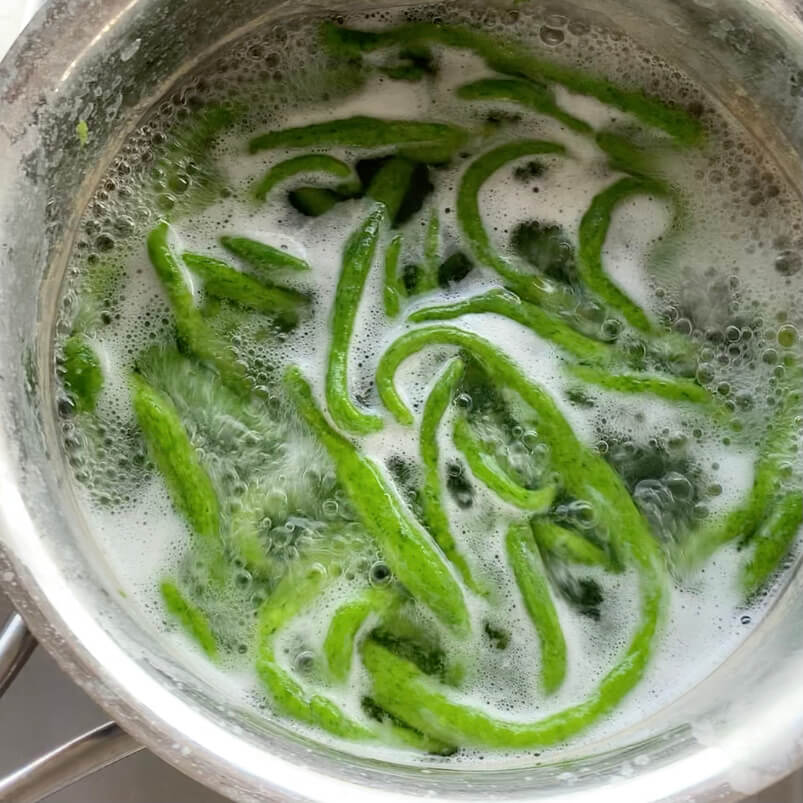 Bright green pici pasta in boiling water