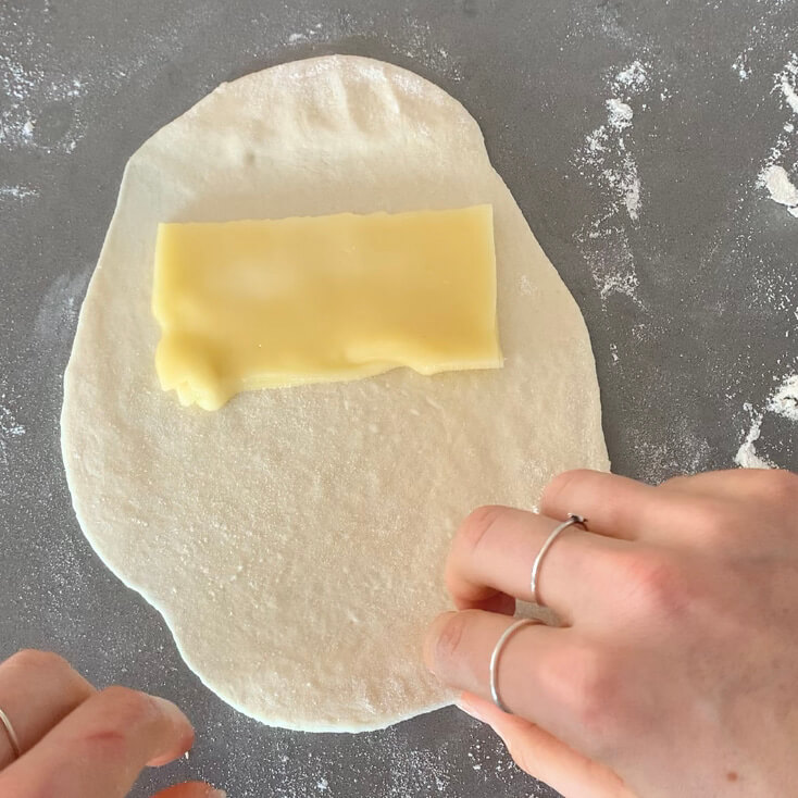 A slice of cheese being folded in between dough