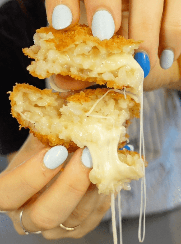 Mozzarella stuffed arancini torn in half with cheese oozing out