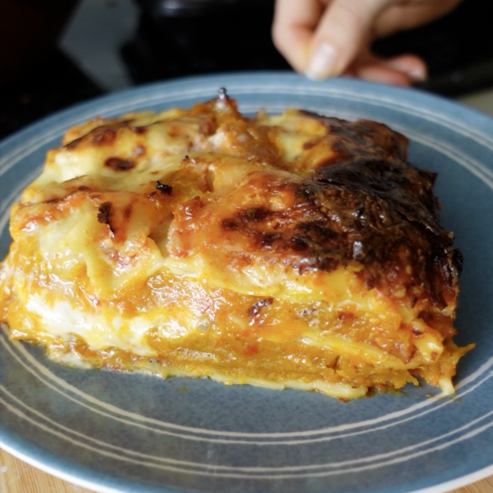 A slice of pumpkin and ricotta lasagne taken from the side to see the layers on a blue plate