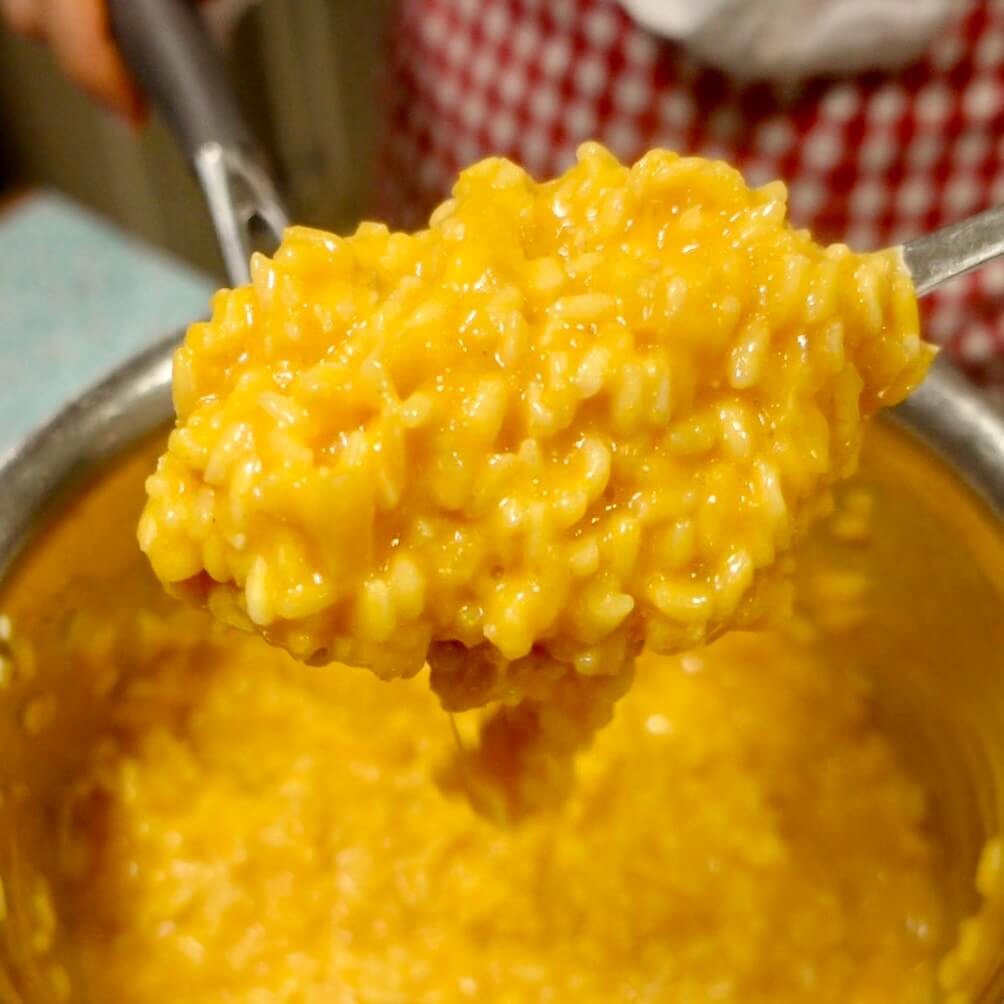 Creamy pumpkin risotto dripping off a serving spoon over a pot full of risotto