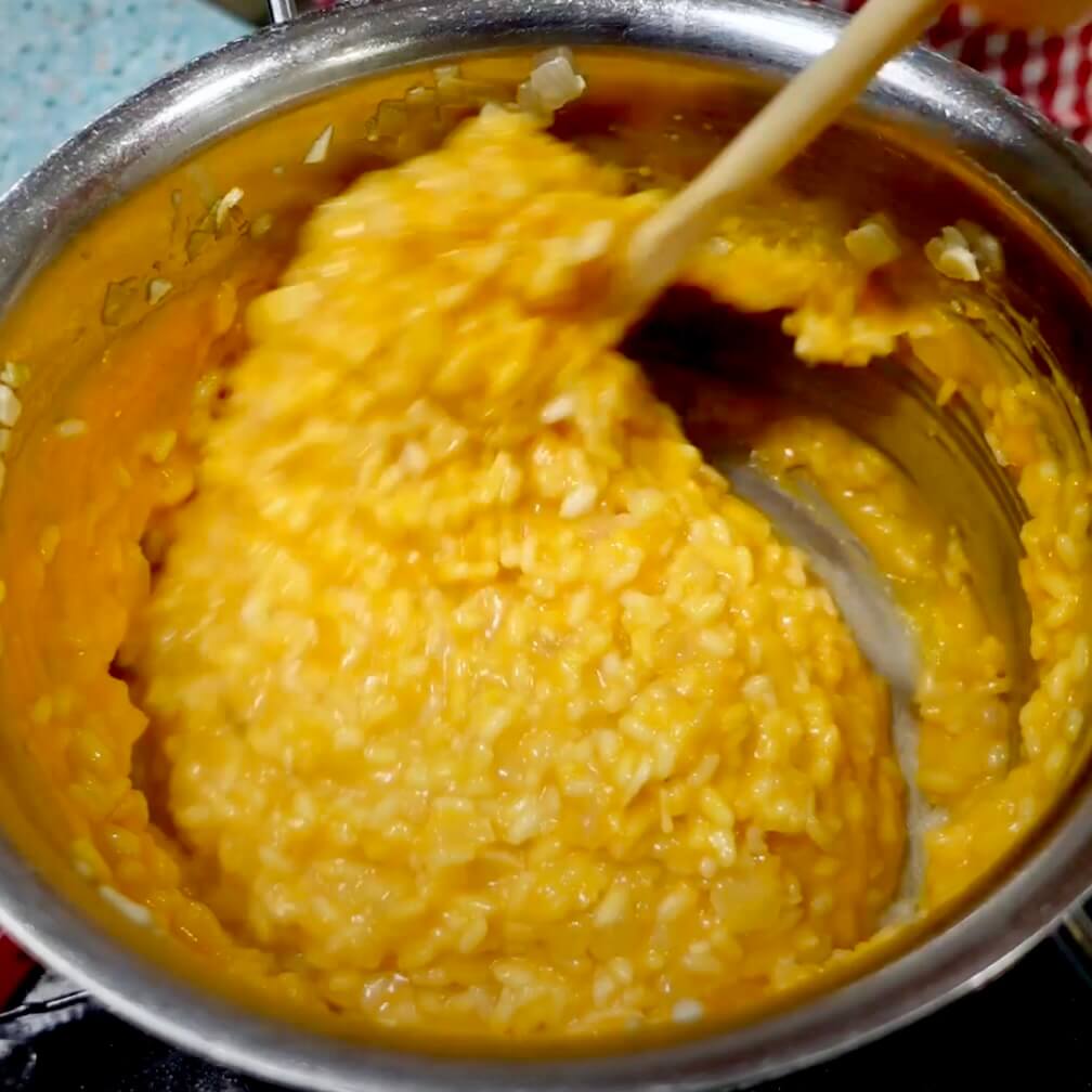 Vigorously stirring pumpkin risotto with a wooden spoon in a stainless steel saucepan