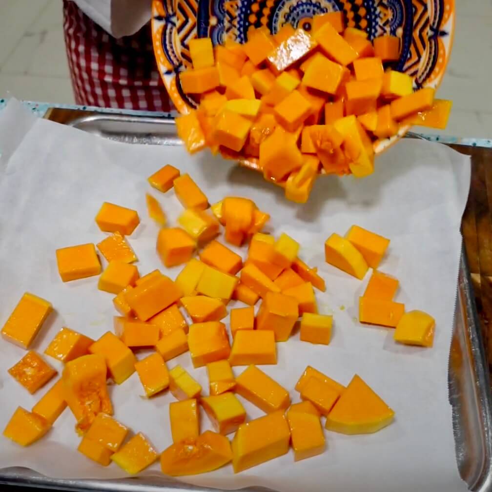 Tipping cubed pumpkin onto a baking tray lined with baking paper