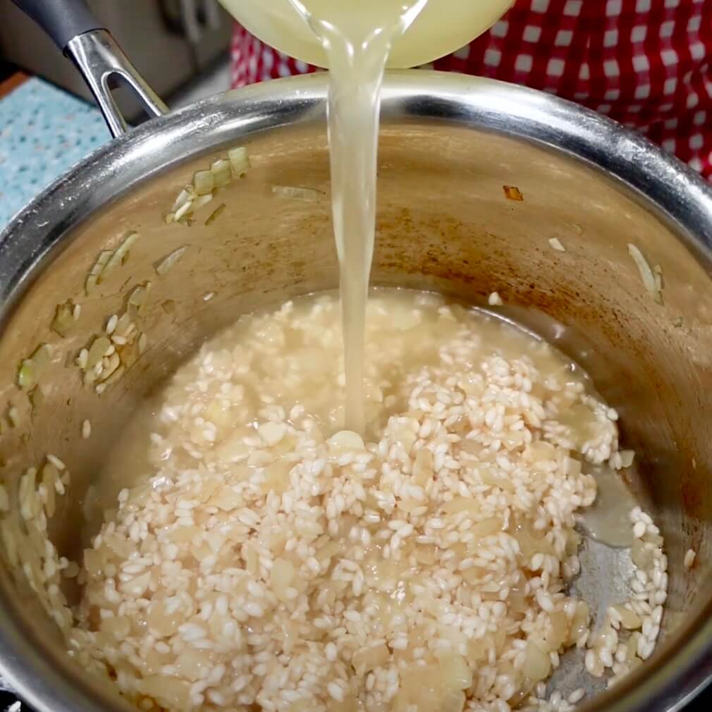 Pouring stock into risotto in a stainless steel saucepan