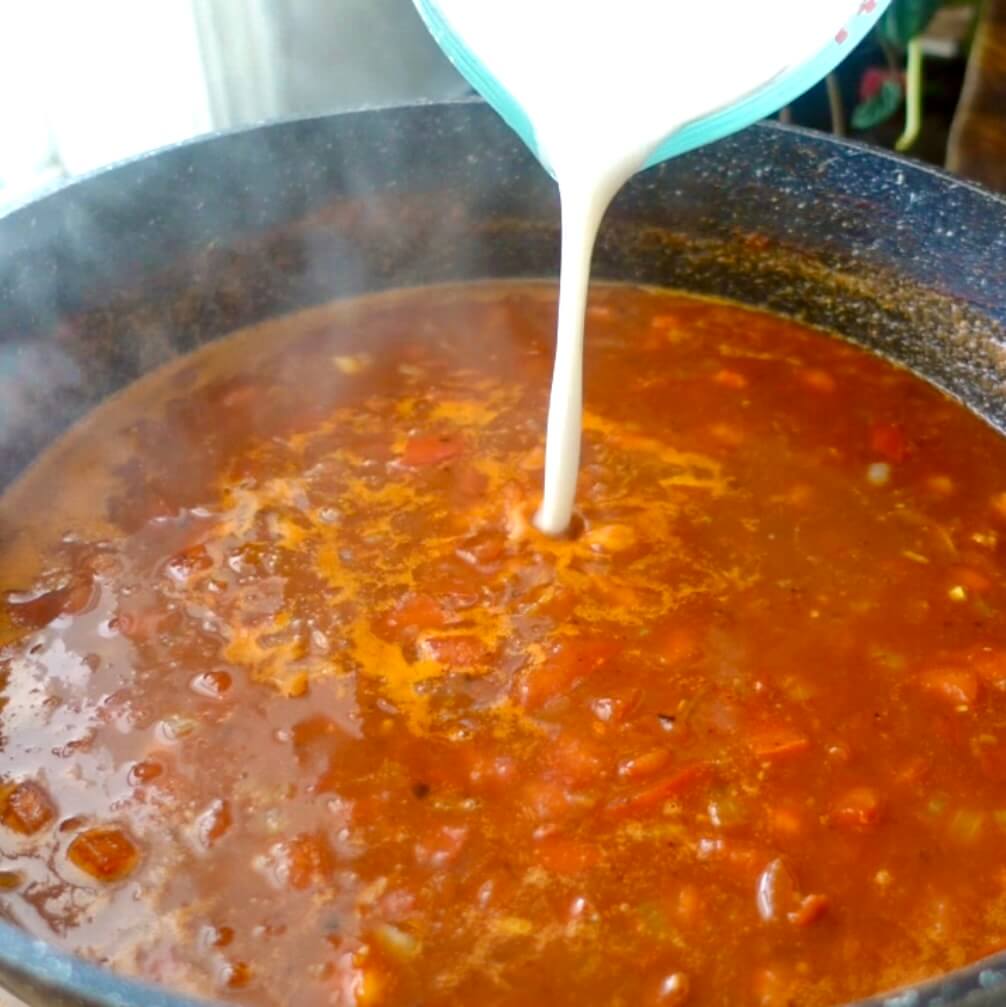 pouring a flour and water mixture into a red sauce to thicken it