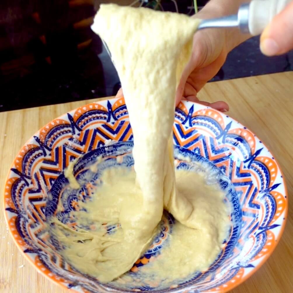 Stretchy hungarian dumpling dough being mixed in an orange and blue bowl with a fork