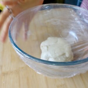 a ball of dough in a glass bowl covered with plastic wrap