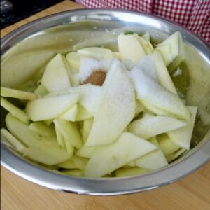 sliced apples in a metal bowl with sugar and cinnamon