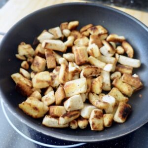 cubes of golden breadcrumbs and hazelnuts in a black frypan