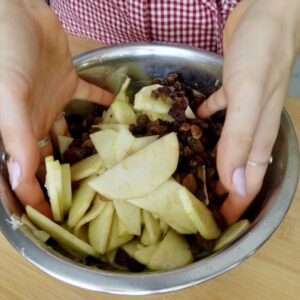 tossing sliced apples with raisins in a metal bowl