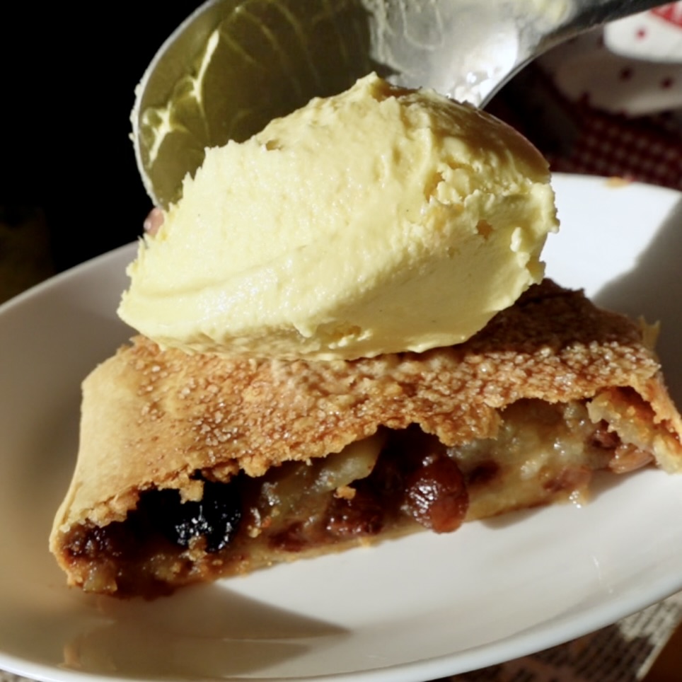 Scooping a quenelle of vanilla ice cream on top of a slice of apple strudel
